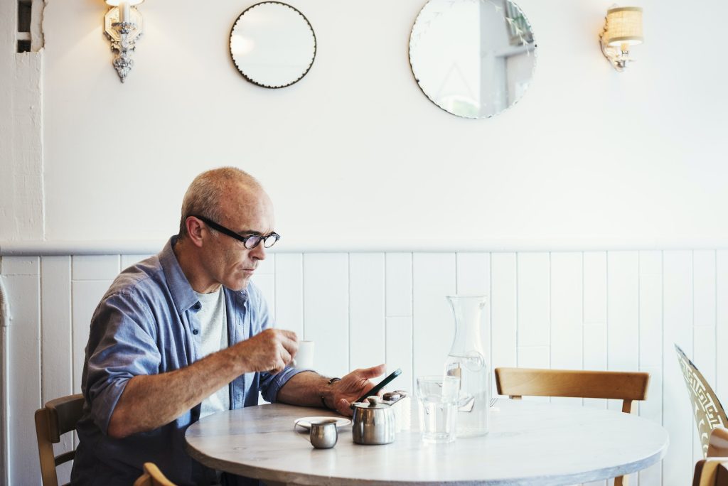 A Man Seated At A Table Checking His Smart Phone Utah Derecho De Familia